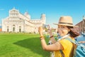 Female traveler in hat with backpack taking photo of the leaning tower in Pisa. Vacation and lifestyle concept Royalty Free Stock Photo