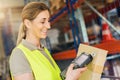 Happy female Worker with barcode scanner, scans bar-code of package, standing at warehouse Royalty Free Stock Photo