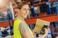 Happy female worker with protective vest and scanner, scans bar-code of package, standing at warehouse of freight forwarding Royalty Free Stock Photo