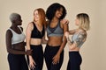 Happy fit sporty diverse girls wearing sportswear talking at beige background.