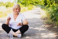 Happy fitness woman sitting on the road in the park with crossed legs and bottle of water near her, looking at the smart Royalty Free Stock Photo