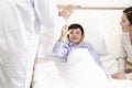 Five year old asian child lying in bed in hospital ward giving doctor a hi-five Royalty Free Stock Photo