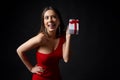 Happy flirting woman in red evening gown holding a gift box