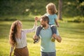 Happy foster family of mother and father carrying adoptive boy child on shoulders, adoption.