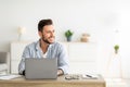 Happy freelance man working on laptop in home office, sitting on workplace and looking aside at free space Royalty Free Stock Photo