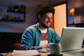 Happy freelancer man working at home with a laptop on a desk at late night. Young guy smiling and browsing on internet Royalty Free Stock Photo