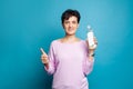 Happy friendly mature woman holding cleaning bottle and showing thumb up on blue background Royalty Free Stock Photo