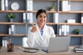 Happy friendly millennial pretty indian female doctor in coat works at laptop and shows thumb up