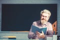 Happy friendly young teacher or post graduate male student standing holding book in front of a blank chalkboard. Royalty Free Stock Photo