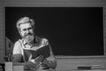 Happy friendly young teacher or post graduate male student standing holding book in front of a blank chalkboard. Royalty Free Stock Photo