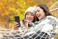 Happy friends checking smart phone in a hammock in autumn Royalty Free Stock Photo