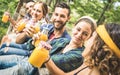 Happy friends drinking healthy orange fruit juice at countryside picnic - Young people millennials having fun together outdoors