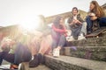 Happy friends drinking paper cup coffee take away on city staircase - Young people having fun outdoor in university break -