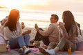 Happy friends eating sandwiches at picnic on beach