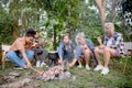 Happy friends group doing recreation with man playing guitar while friends and children grill marshmallow at camping. Royalty Free Stock Photo