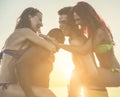 Happy friends having fun on beach at sunset - Young couples playing on summer vacation doing piggyback at Ibiza - Friendship and