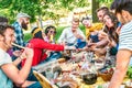 Happy friends having fun outdoor eating snack and drinking red wine at bbq picnic - Young multiracial people enjoying summer time