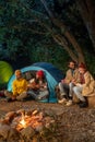 Happy friends having fun together enjoying bonfire camping playing guitar in nature at night. Royalty Free Stock Photo