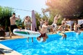 Happy friends jumping and splashing in swimming pool with inflatable floats in luxury resort. Young people in swimwear Royalty Free Stock Photo