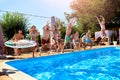 Happy friends jumping and splashing in swimming pool with inflatable floats in luxury resort. Young people in swimwear Royalty Free Stock Photo