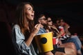 Happy friends sitting in cinema watch film eating popcorn.