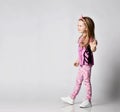 Happy frolic blonde kid girl in summer clothing colorful pants and t-shirt walks looking at copy space. Side view