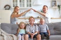 Happy full family with three kids sitting on sofa, mom and dad making roof figure with hands arms over heads. New Royalty Free Stock Photo