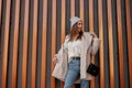 Happy fun young woman in a fashionable hat in a knitted vintage sweater in blue jeans in a stylish warm eco fur coat with a trendy Royalty Free Stock Photo