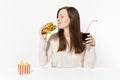 Happy fun young woman sitting at table with burger, french fries, cola in glass bottle isolated on white background Royalty Free Stock Photo