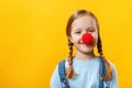 Happy funny child clown with a red nose. Cheerful little girl on a yellow background. April 1st Fools Day. Copy space Royalty Free Stock Photo