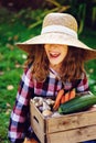 Happy funny child girl in farmer hat and shirt playing and picking autumn vegetable harvest