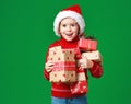 Happy funny child girl in red Christmas hat   with gift on green   background Royalty Free Stock Photo