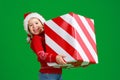 Happy funny child girl in red Christmas hat   with gift on green   background Royalty Free Stock Photo