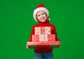 Happy funny child girl in red Christmas hat   with gift on green   background Royalty Free Stock Photo