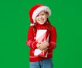 Happy funny child girl in red Christmas hat   with gift on green   background Royalty Free Stock Photo