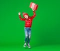 Happy funny child girl in red Christmas hat   with gift jumping on green   background Royalty Free Stock Photo