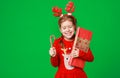 Happy funny child girl in red Christmas reindeer costume with gift on green   background Royalty Free Stock Photo