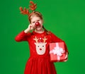 Happy funny child girl in red Christmas reindeer costume with gift on green   background Royalty Free Stock Photo