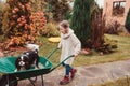 Happy funny child girl riding her dog in wheelbarrow in autumn garden, candid outdoor capture Royalty Free Stock Photo