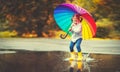 Happy funny child girl with umbrella jumping on puddles in rubb Royalty Free Stock Photo