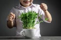 Happy funny child takes care of microgreen in a cup, boy eats pea microgreen. Little gardener at home. Vegan and healthy eating