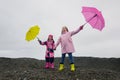 Happy funny children with pink and yellow umbrella outdoors. Girls wearing pink raincoat and enjoying rainfall.