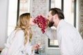 Happy funny couple in bathrobes eating fresh fruits, biting grape together, sitting on the bed in hotel room Royalty Free Stock Photo