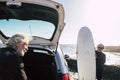 Happy and funny couple of seniors preparing their surftables in the car to go to the beach and trying their first class of surf - Royalty Free Stock Photo