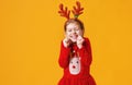 Happy funny emotional child girl in red Christmas reindeer costume on yellow background