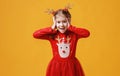 Happy funny emotional child girl in red Christmas reindeer costume on yellow background