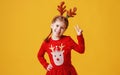 Happy funny emotional child girl in red Christmas reindeer costume on yellow background