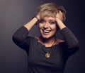 Happy funny emotional excited woman with short blond bob hairstyle in grey blouse and orange fashion necklace on gray background.