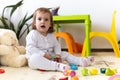 happy funny kid curly baby girl with educational toy blocks flowers. Children play at day care or preschool. Mess in Royalty Free Stock Photo