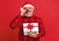 Happy funny senior man in santa hat with gift box holding red christmas tree ball in front of nose Royalty Free Stock Photo